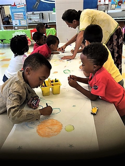 Kids drawing a big mural with their teacher in Spanish class